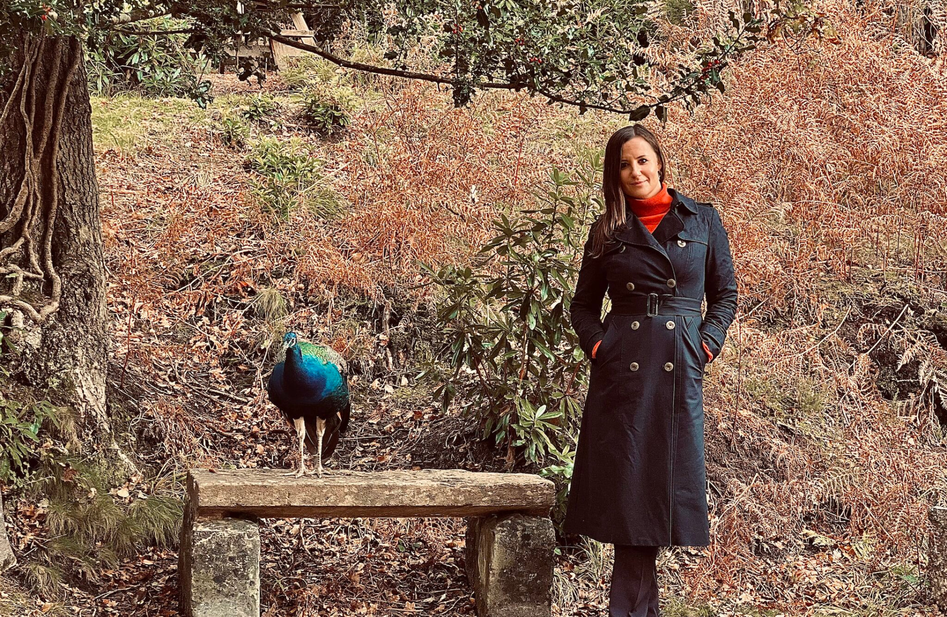 Sylvana Kozak standing outdoors beside a peacock